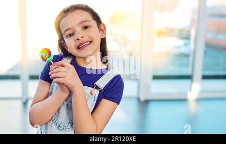 Das süßeste Gesicht der Welt. Porträt eines bezaubernden kleinen Mädchens, das zu Hause einen Lutscher hält. Stockfoto