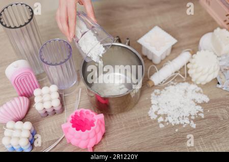 Hobby- und Freizeitkonzept: Frau, die zu Hause Kerzen herstellt, Nahaufnahme der weiblichen Hand, die Sojawachs in die Pfanne gießt Stockfoto