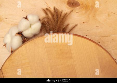 Flauschige dekorative Stacheln und Baumwollblumen auf Holzhintergrund mit Kopierraum. Grußkarte mit rustikalem Holzcharme und weicher Flora. Stockfoto