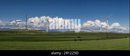 Windmühlen in den Bergen. Bergkette mit grünem Gras, weiße flauschige Wolken am blauen Himmel. Stockfoto