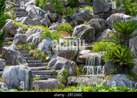 Ein Terrassengarten mit großen Felsen, eine gewundene Steintreppe und ein Wasserfall im Chinese Gardens of Friendship in Sydney, Australien Stockfoto