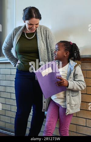 Sie kommt als Nächstes mit ihrer Klassenpräsentation. Ein Mädchen aus der Grundschule steht neben ihrem Lehrer und liest vor ihrer Klasse. Stockfoto