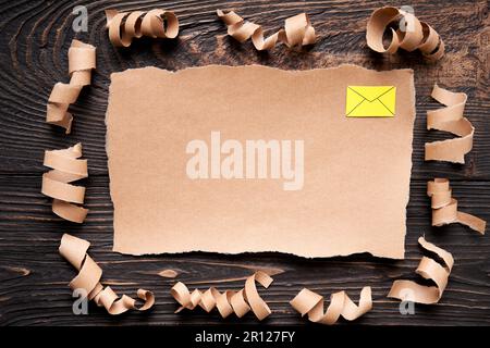 Zerrissenes Blatt Papier mit E-Mail-Symbol, Papierkunststil. Grußkarte, Brief, Einladungsmodell auf dunklem Holzhintergrund. Flach liegend, Draufsicht, kopieren Stockfoto
