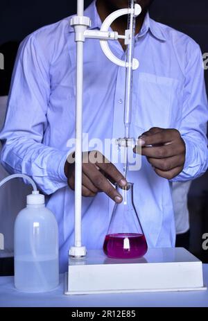 Der Student führt eine Säure-Basen-Titration durch, misst und fügt Lösungen mit Präzision bis zur Neutralisierung hinzu. Dieses Experiment hilft beim Erlernen von Chemis Stockfoto