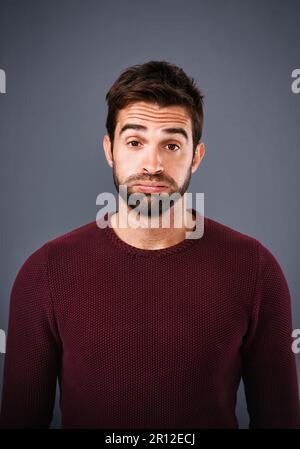 Ich brauche einen emotionalen Schub. Studiofoto eines gutaussehenden jungen Mannes, der vor grauem Hintergrund traurig aussieht. Stockfoto