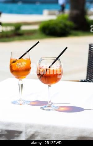 Zwei Gläser aperol Spritz und Campari-Orangencocktails mit Orangenscheiben und Eis auf einem Restauranttisch an einem sonnigen Tag an der Küste. Urlaub CO Stockfoto