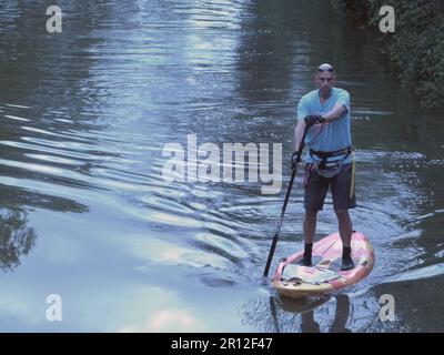 Auf einem Paddelbrett auf einem Kanal nahe Wootton Wawen bei Stratford-upon-Avon Warwickshire balanciert dieser einsame, reife Mann Stockfoto