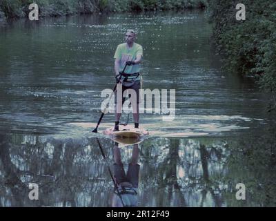 Auf einem Paddelbrett auf einem Kanal nahe Wootton Wawen bei Stratford-upon-Avon Warwickshire balanciert dieser einsame, reife Mann Stockfoto