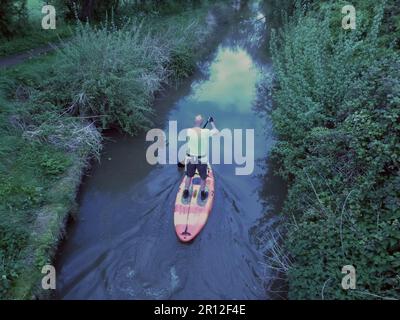 Auf einem Paddelbrett auf einem Kanal nahe Wootton Wawen bei Stratford-upon-Avon Warwickshire balanciert dieser einsame, reife Mann Stockfoto