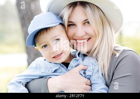 Schwangere Mutter und ihr kleiner Sohn gehen und umarmen im Wald und haben lustige Zeit miteinander verbracht Stockfoto