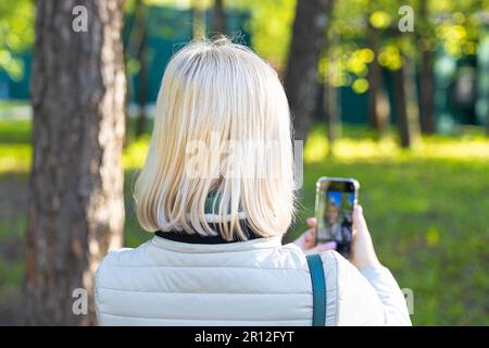 Frau macht Selfie auf Smartphone im Park. Ein Mädchen, das sich am Telefon filmt Stockfoto