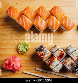 Ein hölzernes Schneidebrett mit zwei Sushi-Sorten, kunstvoll arrangiert, begleitet von zwei Essstäbchen Stockfoto