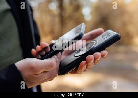 Nahaufnahme der Hände eines Mannes, der ein modernes Smartphone und eine kabellose Powerbank hält, isoliert auf weißem Hintergrund Stockfoto