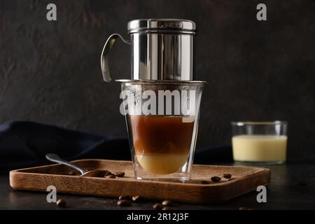 Zubereitung von traditionellem vietnamesischem Kaffee mit Kondensmilch in einer Glasbecher auf schwarzem Hintergrund. Schließen. Stockfoto