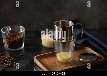 Traditionelles Verfahren zur Herstellung von vietnamesischem Kaffee mit süßer Kondensmilch in Glasbecher auf schwarzem Hintergrund. Schließen. Stockfoto