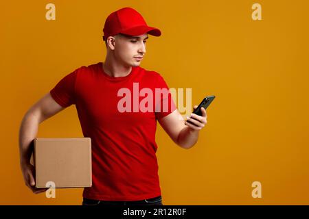 Angestellter des Lieferers in roter Mütze, T-Shirt mit leerem Karton und Telefon Stockfoto