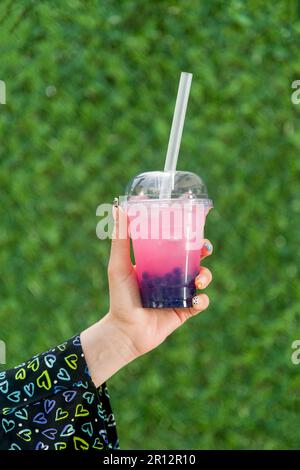 Eine Frau mit Seifenblasentee und Limonade vor der grünen Graswand Stockfoto