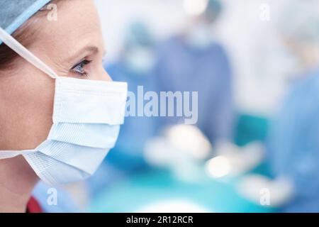 Streben nach einem erfolgreichen Operationsergebnis. Seitenprofil einer reifen Ärztin, die Krankenhaus-Peelings und eine schützende Gesichtsmaske trägt - Copyspace. Stockfoto