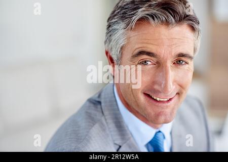 Niemals aufgeben, auch nicht, nachdem Ergebnisse erzielt wurden. Porträtfoto eines selbstbewussten, reifen Geschäftsmannes, der lächelt und einen Anzug drinnen trägt. Stockfoto
