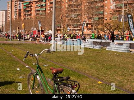 Ein grüner Schritt durch das Fahrrad neben weggeworfenen Plastikflaschen im Vordergrund der Leute, die den Barcelona Marathon auf den Straßen der Stadt auf einem heißen Lauf laufen Stockfoto