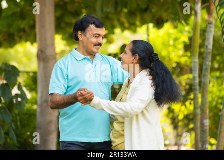 Glückliches indisches Seniorenpaar, das im Park Hand hält und zusammen tanzt - Konzept des Vergnügens, Stockfoto