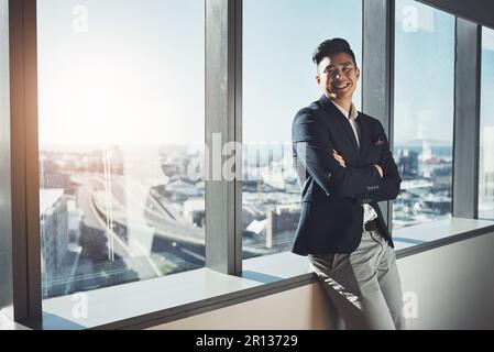 Er ist eine führende Führungskraft im Business Imperium. Porträt eines jungen Geschäftsmannes, der am Fenster eines Büros steht. Stockfoto