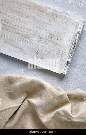 Ein weißes Holztablett und eine grobe Leinenserviette auf einem grauen Betontisch. Draufsicht mit Kopierbereich Stockfoto