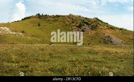 Wunderschöne Aussicht von unten auf den Hügel und die Wolken an einem sonnigen Sommertag. Gras, Bäume und viele Steine wachsen auf Hügeln. Kleine Steine gießen in nicht-wea herunter Stockfoto