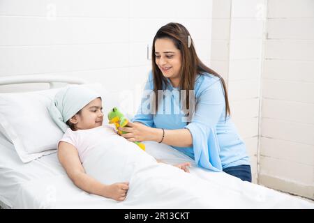 Indische Frau mit Spielzeug besucht ihre kleine Tochter oder Krebspatient, die sich einer Chemotherapie im Krankenhaus unterziehen. Gesundheitskonzept. Stockfoto