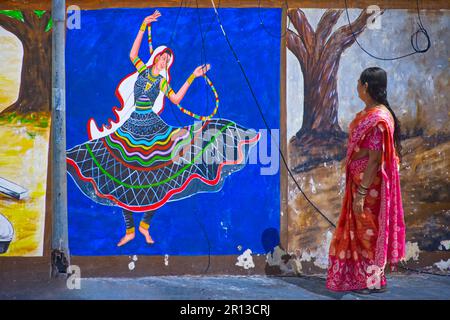 Eine indische Frau in Sari, die in der Nähe eines wunderschönen Wandbildes spaziert und eine Tänzerin repräsentiert Stockfoto