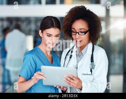 Die Ergebnisse sehen gut aus. Zwei fokussierte junge Ärzte arbeiten gemeinsam an einem digitalen Tablet, während sie tagsüber im Krankenhaus stehen. Stockfoto