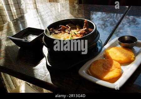 Traditionelles koreanisches Gericht. Bibimbap in einer beheizten Steinschale und gebratenen Sojabohnengaletten. Stockfoto