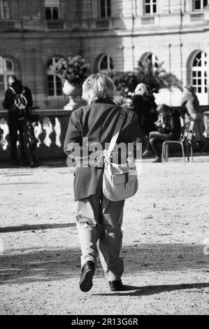 Eine alte Dame, die im Luxemburger Garten spaziert. Rückansicht. Urbane Szene. Paris (Frankreich) Selektive Fokussierung auf die Hände. Schwarz auf Weiß. Stockfoto