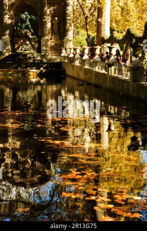 Herbst in Paris. Jardin Du Luxembourg. Touristen und Bürger, die sich in der Nähe des Medici-Brunnens in goldenen Sonnenstrahlen entspannen. Selektiver Fokus auf Reflexion. Stockfoto