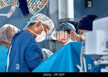 Das Team von Chirurgen im Operationssaal hat sich über den Patienten gebeugt, komplexe chirurgische Operationen, High-Tech-Medizin, lebensrettend. Stockfoto