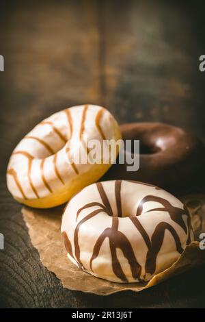 Weiße und dunkle Schokoladen-Donuts auf einem dunklen Holztisch, vertikal mit Kopierbereich Stockfoto