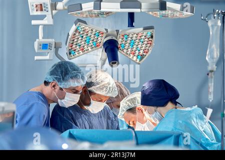 Das Team von Chirurgen im Operationssaal hat sich über den Patienten gebeugt, komplexe chirurgische Operationen, High-Tech-Medizin, lebensrettend. Stockfoto