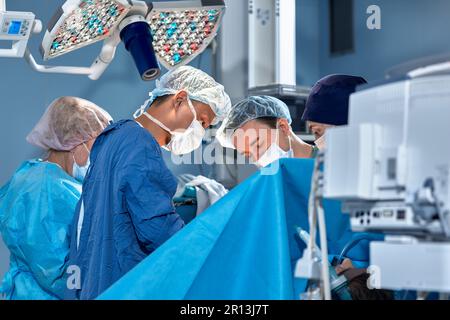 Das Team von Chirurgen im Operationssaal hat sich über den Patienten gebeugt, komplexe chirurgische Operationen, High-Tech-Medizin, lebensrettend. Stockfoto