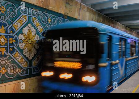Slow-Shutter-Foto eines leicht verschwommenen Zuges, der an der bunt gemusterten Pakhtakor-U-Bahnstation ankommt, um die Baumwollpflückindustrie zu feiern Stockfoto