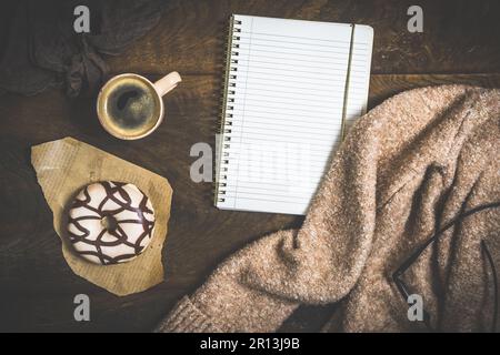 Donut, Kaffee und ein Notizbuch auf einem dunklen Holztisch, gemütliche Szene einer Kaffeepause, Draufsicht mit Kopierbereich Stockfoto