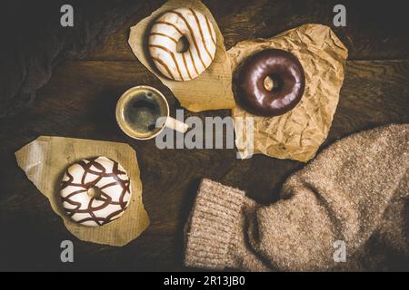 Schokoladen-Donuts und Kaffee auf einem dunklen Holztisch, gemütliche Szene einer Kaffeepause, Blick von oben Stockfoto