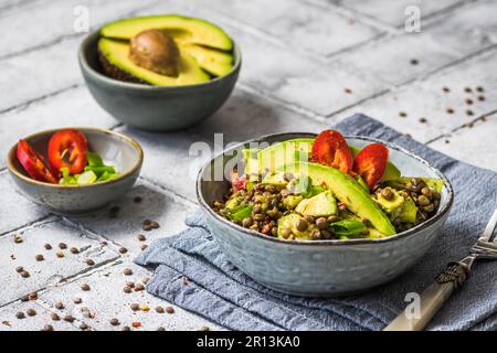 Linsensalat mit Avocado und rotem Pfeffer auf grauem Hintergrund. Vegetarische und vegane Speisen. Stockfoto