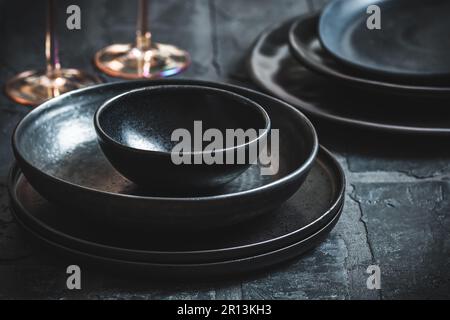 Teller und Schüsseln aus schwarzem Steingut auf einem rustikalen schwarzen Tisch Stockfoto