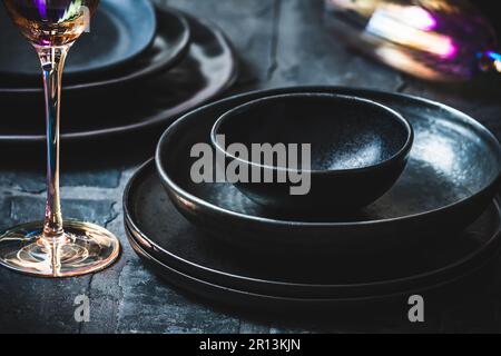 Schwarzes Steingut und pinkfarbene Champagnergläser auf einem rustikalen schwarzen Tisch Stockfoto