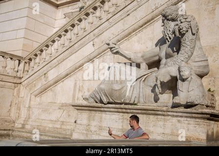 Ein Mann sitzt vor einer Statue eines römischen gottes mit einem Tisch in der Hand Stockfoto