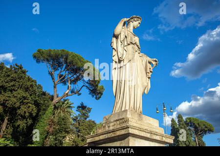 Die Statue einer Frau mit einem lang fließenden Kleid steht vor einem blauen Himmel. Rom, Italien Stockfoto