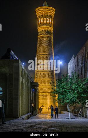 Nachtszene des mit Flutlicht beleuchteten großen Minaretts Kalon, das über die engen Gassen von bukhara usbekistan ragt Stockfoto