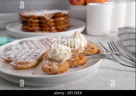 Frisch gebackene Waffeln mit Puderzucker und Schlagsahne auf dem Küchentisch Stockfoto