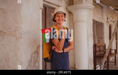 Touristenausflug in die Altstadt von Dubai, Vereinigte Arabische Emirate. Asiatische Frau mit der Flagge der Vereinigten Arabischen Emirate in alten engen Straßen von Bur Dubai und Creek, Al Seef Heritage Souk. Reise- und Stockfoto