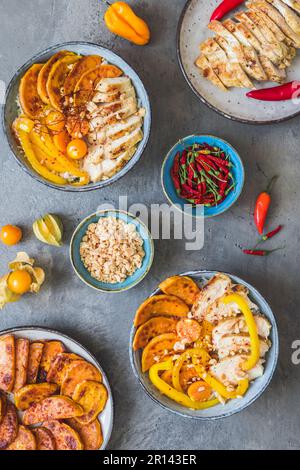 Zwei buddha-Schüsseln mit scharfem Huhn, Reis, Paprika, Süßkartoffel und gehackten Erdnüssen, Trend und gesundem Essen, Draufsicht auf grauem Hintergrund Stockfoto